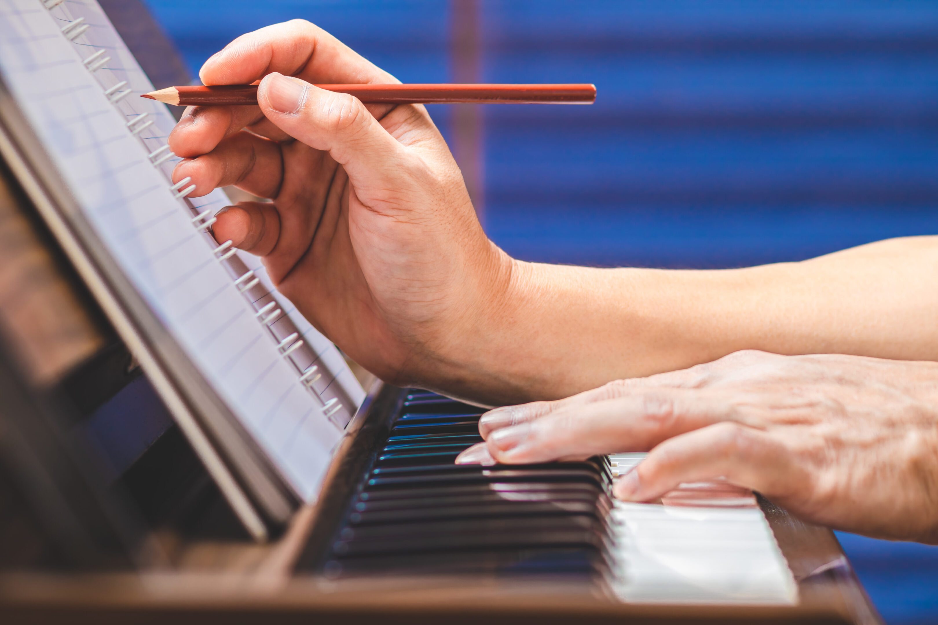 close up male musician hand writing a hit song while playing acoustic piano. songwriting concept A person is playing piano with a pencil